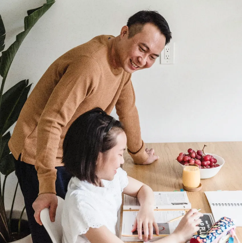Asian father looking over his daughter studying, offering her snacks