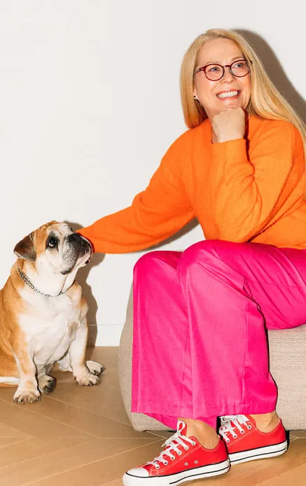 Target customer image: Long-haired women in 40-50s in bright orange and pink clothes, sitting on a couch and petting her dog